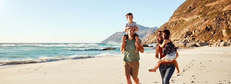 Junge Familie läuft am Strand, die Mutter trägt die Tochter am Arm und der Vater trägt den Sohn auf den Schultern.
