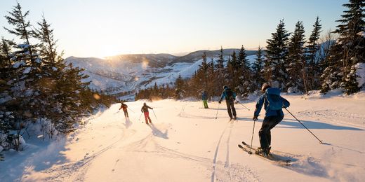 Skifahrer auf der Piste bei Sonnenuntergang mit Blick auf die verschneiten Berge